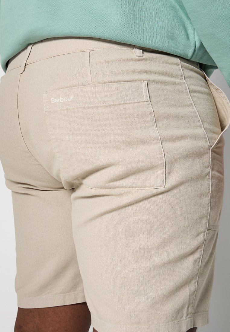 Beżowe bawełniane szorty o teksturowanym wykończeniu, z tylną kieszenią i białym logo "Barbour". Casualowy design z śrenią wysokością w pasie.
