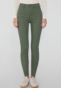 Jean skinny vert à taille haute, en tissu lisse. Comprend des poches avant, une fermeture à bouton et des coutures contrastées.