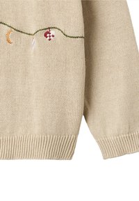 Pull beige en maille avec poignets et ourlet côtelés. Présente une broderie décorative de croissant de lune, d'ornement et de motif damier.