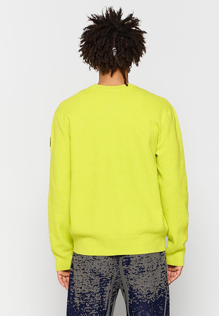 Maglione a coste verde lime con collo rotondo, dotato di maniche lunghe e vestibilità aderente. Abbinato a pantaloni scuri con un motivo testurizzato.