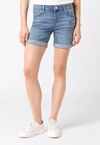 Jasnoniebieskie szorty dżinsowe z podwiniętymi nogawkami, pięcioma kieszeniami i zapięciem na guzik. W połączeniu z białymi trampkami. Gładka tekstura.