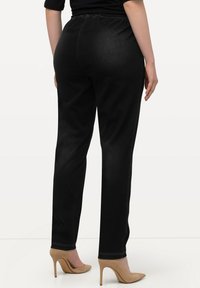 Pantalones vaqueros negros con cintura elástica, diseño de pierna recta y detalles de costura mínimos, combinados con tacones altos beige.