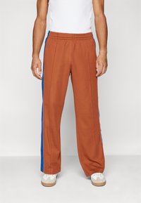 Bruine sweatpants met blauwe zijpanelen, elastische tailleband en rechte broekspijpen. Gemaakt van een zachte stof, geschikt voor casual kleding.
