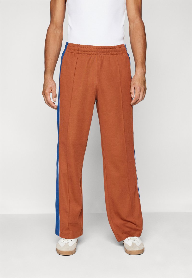 Bruine sweatpants met blauwe zijpanelen, elastische tailleband en rechte broekspijpen. Gemaakt van een zachte stof, geschikt voor casual kleding.