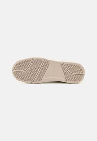 Suola delle scarpe di colore chiaro con un motivo di grip testurizzato. Presenta bordi curvi e un marchio al centro. Design liscio e piatto per una maggiore stabilità.