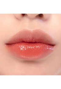 Labios llenos y suaves cubiertos con un producto labial brillante de color coral. La textura parece suave, con un sutil brillo y reflejo de luz.