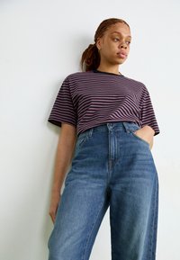 Top a maniche corte a righe in viola e nero, abbinato a jeans blu a vita alta. Tessuto morbido, vestibilità comoda e scollatura semplice.