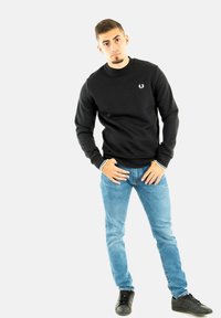 Sudadera negra con cuello redondo, puños acanalados con acentos blancos, jeans slim-fit azules y zapatillas negras. Sin patrones ni logotipos visibles.