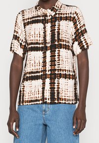 Chemise à manches courtes en tissu léger avec un motif tie-dye abstrait dans des tons de beige, marron et noir, dotée d'un col.