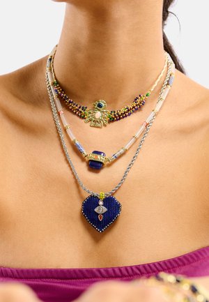 Colliers de perles dorées, bleues et multicolores ; l'un présente un pendentif en forme de cœur avec un motif d'œil, design superposé avec des textures variées.