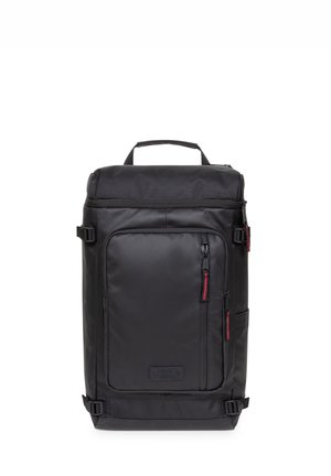 Mochila rectangular negra con asa superior, bolsillo frontal con cremallera con tiradores rojos y correas laterales ajustables.