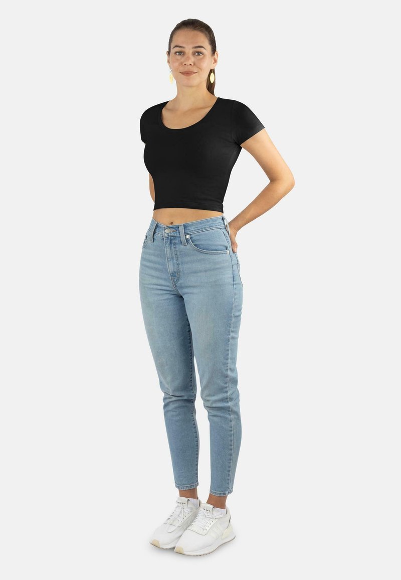 Schwarzes, verkürztes T-Shirt kombiniert mit hellblauen, enganliegenden Jeans mit hoher Taille und weißen Sneakern, vor einem schlichten Hintergrund.