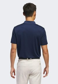 Marineblauwe polo met korte mouwen en een ontspannen pasvorm, gemaakt van een gladde stof. Gekleed met lichtgekleurde broeken en een riem.