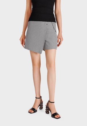 Donna che indossa una canotta nera senza maniche, una gonna asimmetrica a quadri bianco e nero e sandali neri con tacco scolpito.