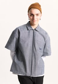 Striped short-sleeve shirt in navy and white with a zip front and collar. Features a chest pocket with an embroidered logo. Cotton blend material.