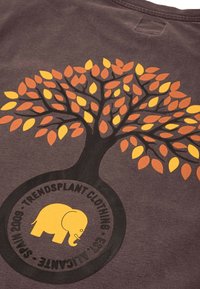 Hnědé tričko se vzorem stromu s oranžovými a žlutými listy a kruhovým logem slona ve žluté barvě na spodní části.