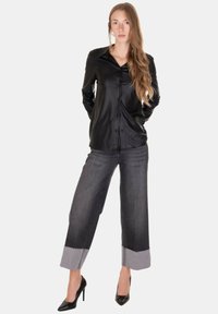 Camicia nera in pelle con bottoni, jeans grigi a gamba larga con orlo a contrasto e décolleté nere. Tessuto liscio e design elegante.