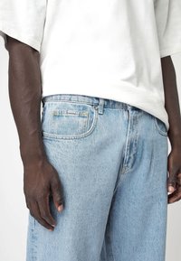 Lichtblauwe denim jeans met een relaxed fit, met een klassiek vijf-pocket ontwerp en gele stiksels op de zakken. Gecombineerd met een wit T-shirt.