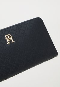 Portafoglio blu navy realizzato in materiale testurizzato con un motivo geometrico. Accentua il logo in tono oro, ben visibile sul fronte.