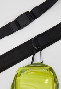 Transparent gul bag med en sort rem med plastspenne og en metallkarabin, som fremhever en glatt tekstur og funksjonelt design.