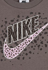 Pilkas džemperis su ryškiu juodu ir rožiniu Nike logotipu su gyvūnų rašto akcentais, priešingos tekstūruoto fono su tamsiomis dėmėmis.