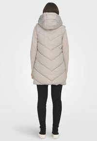 Gilet imbottito grigio chiaro con un motivo a zigzag, dotato di cappuccio. Indossato sopra un maglione leggero, abbinato a leggings neri e scarpe.