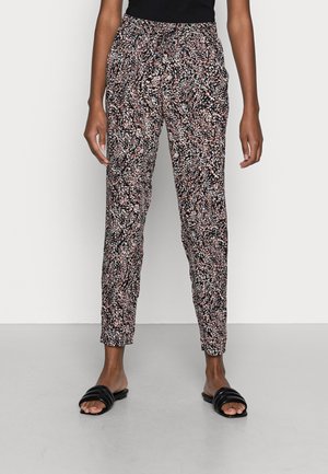 Femme portant un pantalon slim taille haute avec un imprimé abstrait noir, blanc et rose, associé à des sandales slides noires et un top noir.