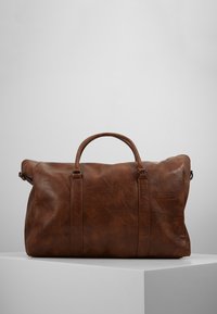 Braune Leder-Duffle-Tasche mit weicher Textur, runden Griffen und verstellbaren Schulterriemen; verfügt über feine Nähte und ein geräumiges Design.