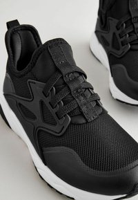 Black athletic shoes with a textured mesh upper, smooth accents, and a cushioned sole. Features a prominent lace system for secure fit.