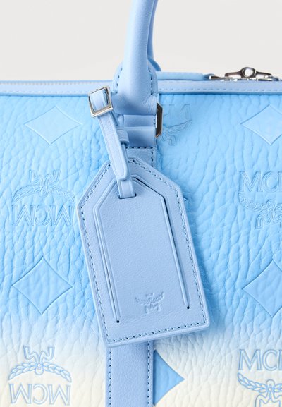Τσάντα χειρός από δέρμα σε ανοιχτό μπλε χρώμα με ανάγλυφα λογότυπα MCM, ραμμένη ταμπέλα αποσκευών και φαίνεται φερμουάρ στην κορυφή.