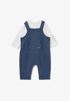 Denim blauwe overall met eronder een witte langemouwen shirt. Voorzien van verstelbare bandjes, twee grote knopen en een voorzak.