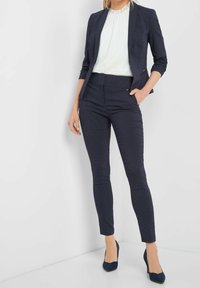 Granatowa marynarka z wyciętym kołnierzem, połączona z dopasowanymi granatowymi spodniami w wzór. Oba elementy cechują się eleganckim, dopasowanym krojem i teksturowaną tkaniną.