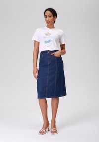 Jeans blyantskjørt i mørkeblått, midt-lengde, med frontlommer og kontraststing. Kombinert med en hvit grafisk t-skjorte.