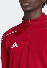 Giacca sportiva rossa con zip, dettagli bianchi e pannello spessorato sulle spalle. Presenta un colletto e una breve zip al collo.