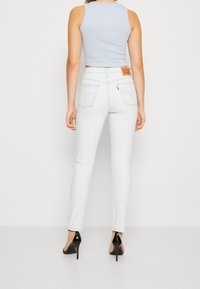 Jeans de denim blanco con un corte ajustado y detalles de costura sutiles en los bolsillos traseros; combinados con una camiseta sin mangas cortada de color azul claro y tacones negros.