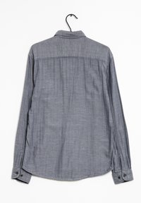 Pitkähihaista paitaa harmaasta tekstuurikankaasta. Varustettu terävällä kauluksella, napitettavilla hihansuilla ja kaarevalla helman. Roikkuu mustasta koukusta.