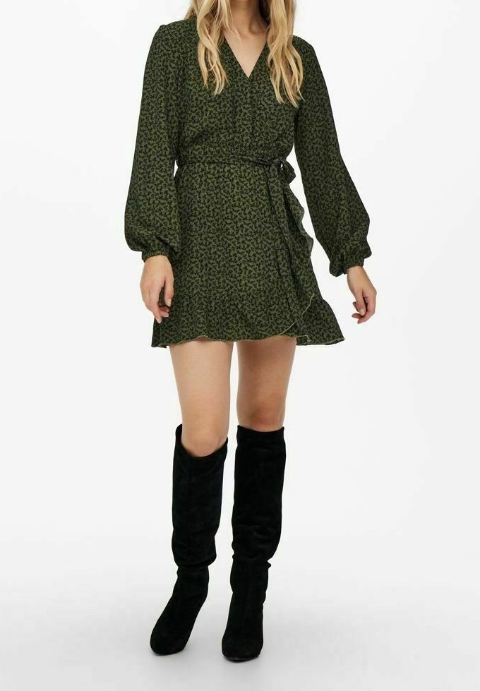 Robe portefeuille verte avec manches longues bouffantes, col en V et motif floral. Assortie à des bottes noires en daim montant jusqu'aux genoux.