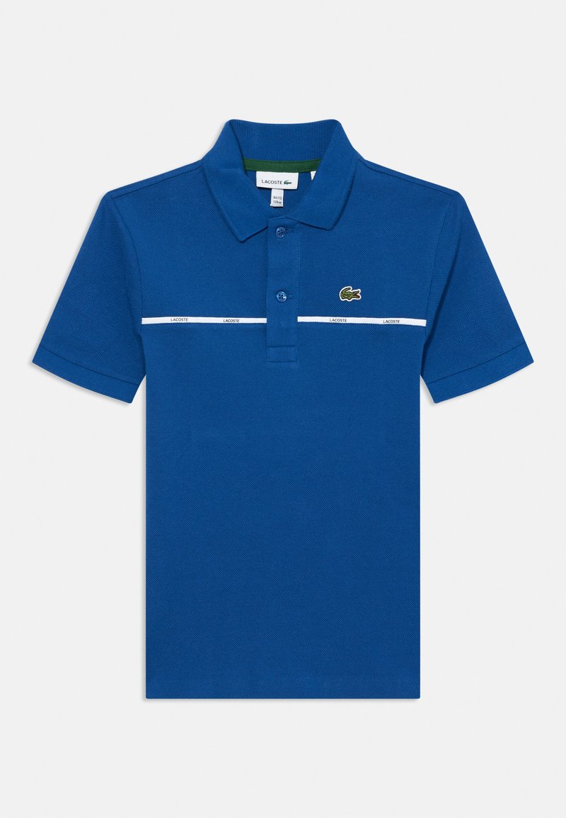 Zils polo krekls, kas izgatavots no teksturēta auduma, ar divu pogu aizdari, baltu svītru ar zīmola nosaukumu un zaļu iekšējo apkakli. Lacoste logo zaļā krāsā.