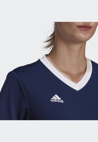 Navy athletic shirt with a white V-neck collar, featuring the Adidas logo in white on the left side. Made from smooth, flexible fabric.