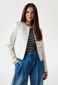 Witte leren jas met gestikte details, gedragen over een zwart-wit gestreept shirt, gecombineerd met hoge taille lichte wijde jeans.