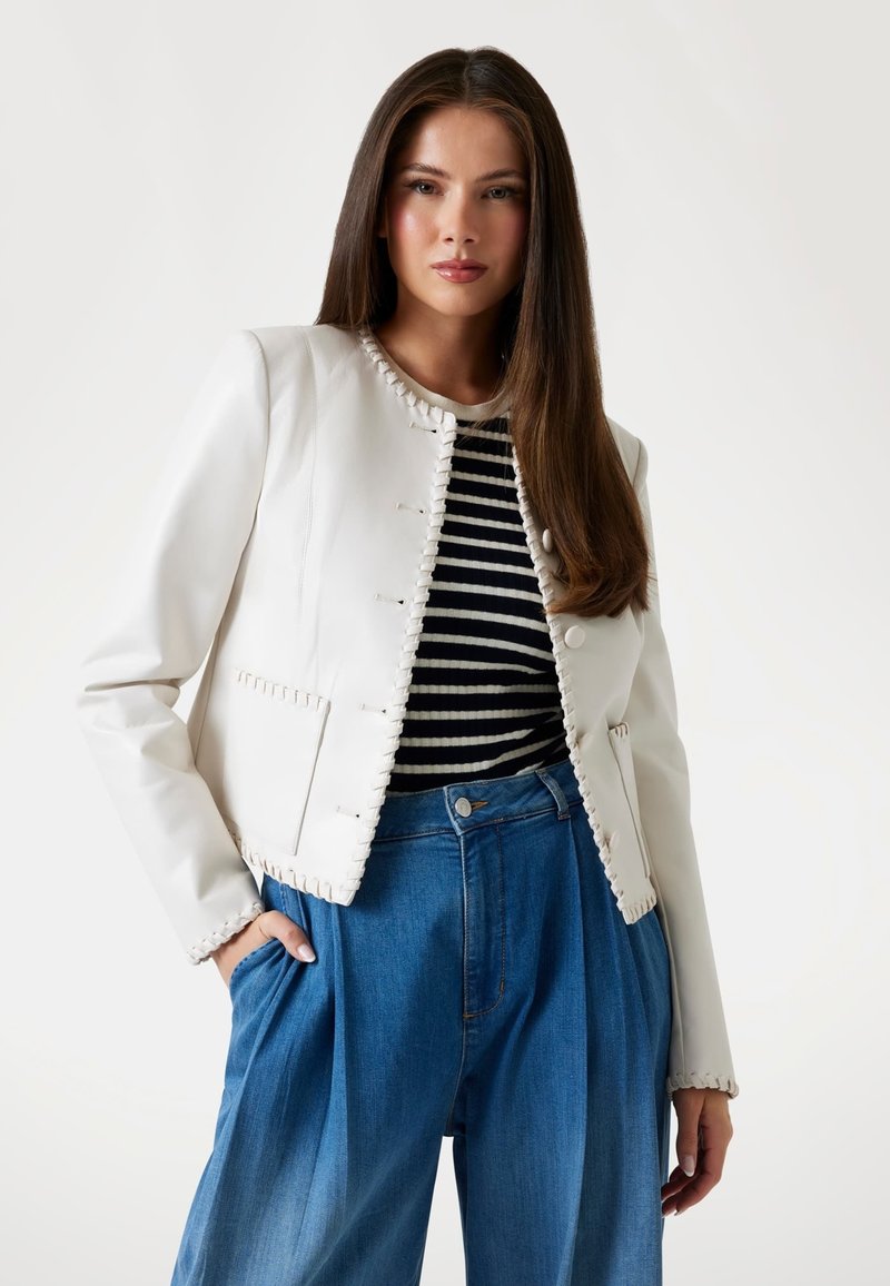Witte leren jas met gestikte details, gedragen over een zwart-wit gestreept shirt, gecombineerd met hoge taille lichte wijde jeans.