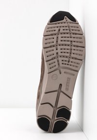 Semelle d'une chaussure Geox beige et noire présentant un dessin de bande de roulement avec des perforations circulaires et le nom de la marque embossé sur la semelle.