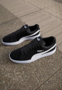 Zwarte sportieve schoenen met een bovenkant van suède, witte accenten en een gestructureerde zool. Voorzien van een vetersluiting en een opvallend merklogo.