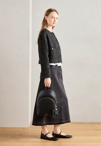 Czarny krótki sweter z teksturowanej tkaniny, szara dżinsowa spódnica maxi, czarna plecak z złotymi akcentami oraz czarne płaskie buty.