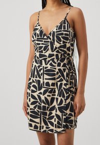 Robe portefeuille en tissu beige avec motifs abstraits noirs, dotée de fines bretelles réglables et d'une ceinture à nouer à la taille.