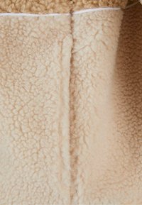 Beige fliisriie, millel on pehme ja udune tekstuur, millel on sile, veidi tõstetud pind ja valge äär üstosas.