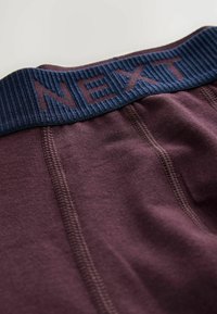 Burgundy boxershorts med en ribbad marinblå midja. "NEXT" är präglat på midjan. Har flatlocksömmar och en mjuk tygtextur.