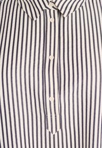 Nööbiga kaelusega särk, millel on vertikaalsed mustad ja valged triibud ning nähtavad valged nööbid keskpaneli all.