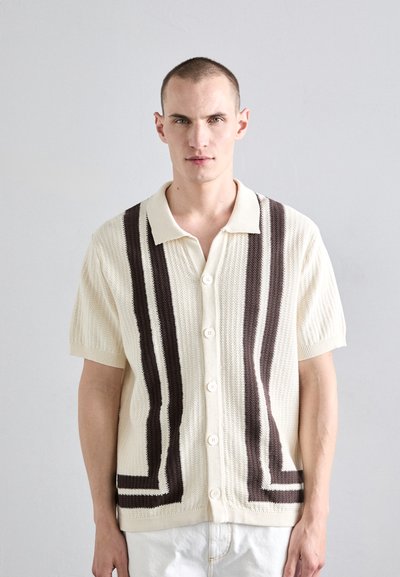 Kurzärmliges Strickshirt in Creme mit vertikalen braunen Streifen. Verfügt über einen Kragen und eine Knopfverschlussgestaltung, strukturierten Stoff und lockere Passform.