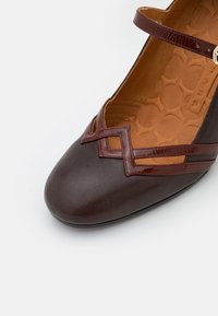 Chaussure en cuir marron avec un bout pointu, dotée d'un design en croix et d'une bride à la cheville, agrémentée de détails brillants marron fonc é.